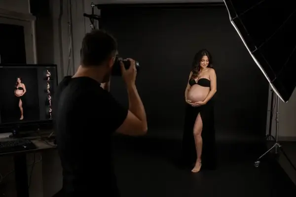 Babybauch Shooting 2 Professionelles Babybauchshooting im Fotostudio München: Ein Fotograf bei der Arbeit mit einer schwangeren Kundin in eleganter schwarzer Lingerie und langem Rock vor einem dunklen Hintergrund mit Profoto-Blitzsystem.