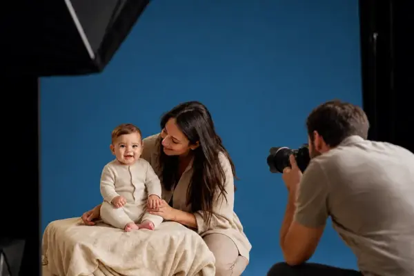 Baby & Kleinkind Fotos 2 Professionelles Baby-Shooting bei PM STUDIOS München: Ein Fotograf fängt das Lachen eines Babys auf einer hellen Decke ein, während die Mutter begleitend zur Seite steht; warmes Licht-Setting im Studio.