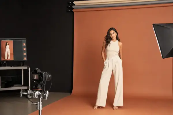 E-Commerce Shooting 2 Professionelle E-Commerce-Fotografie bei PM STUDIOS München: Ein Modell in einem cremefarbenen Outfit posiert vor einem warmen erdfarbenen Hintergrund; Studio-Eindrücke mit professioneller Softbox und Live-Vorschau am Monitor.