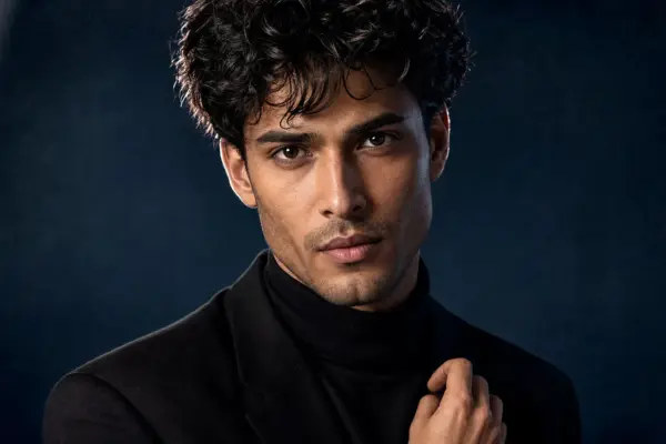 Editorial photography 1 Editorial men's headshot by PM STUDIOS Munich: Intensive close-up portrait of a man with dark curly hair against a textured deep blue studio backdrop, featuring dramatic cinematic lighting.