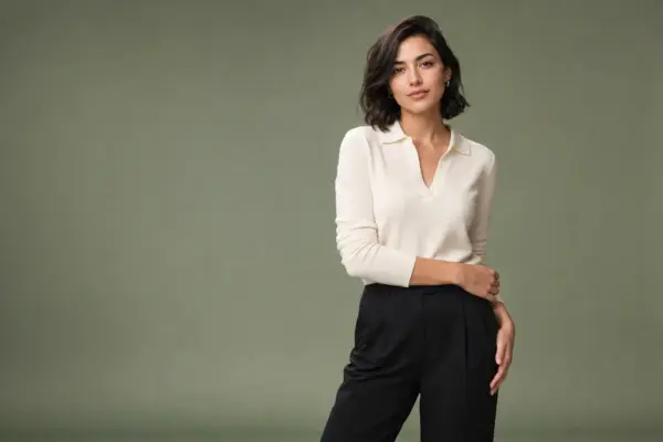 Sedcard Shooting 2 Professionelles Studio-Porträt von PM STUDIOS München: Eine Frau in einem cremefarbenen Poloshirt und schwarzer Hose posiert stilsicher vor einem olivgrünen Hintergrund im Querformat.