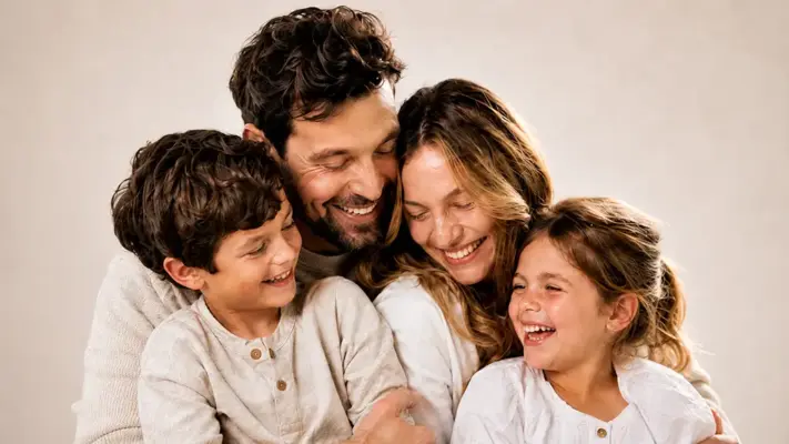 Emotionales Familienporträt von PM STUDIOS München: Eine lachende vierköpfige Familie mit Vater, Mutter, Sohn und Tochter in heller Kleidung posiert eng umschlungen im Fotostudio.