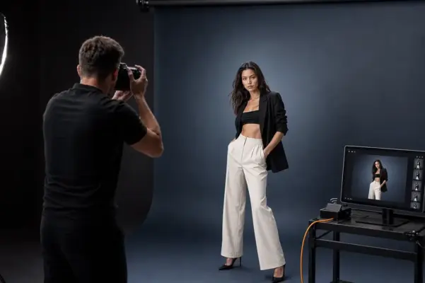 Professionelles Fashion-Shooting bei PM STUDIOS München: Ein Fotograf fotografiert ein Model in kontrastreicher Kleidung (schwarzer Blazer, helle Hose) vor dunkelblauem Hintergrund; inklusive Live-Vorschau am Monitor.