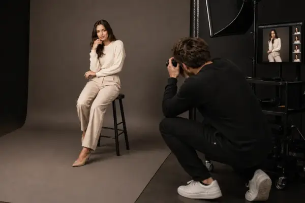 Vouchers 3 Behind the scenes of a professional headshot session at PM STUDIOS Munich: A photographer shooting a seated model against a grey background with live tethered capture on a studio workstation for instant review.
