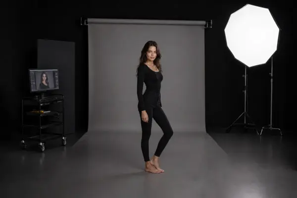 Comp card shooting 1 Wide-angle studio view of a professional model comp card session at PM STUDIOS Munich: Model in black attire posing on a grey backdrop, featuring a high-end Octabox light and live digital review workstation.