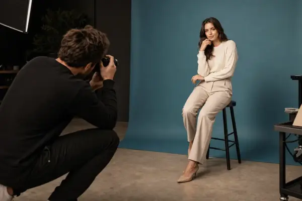 Vouchers 2 Behind the scenes of a professional portrait session at PM STUDIOS Munich: A photographer capturing a woman in a stylish cream outfit against a modern blue-grey studio backdrop.