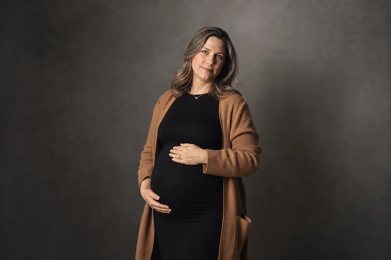 Babybauchshooting in München: So bereitest du deine Studiofotos vor 2 Schwangere Frau mit Strickjacke über schwarzem Kleid beim Babybauchshooting in München